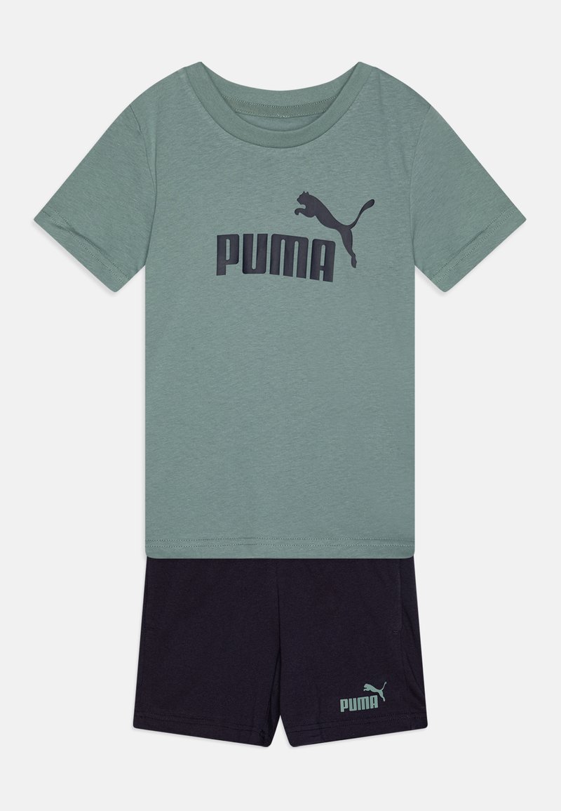 T-shirt verde in cotone con logo "PUMA" blu scuro, abbinato a pantaloni corti scuri con un logo più piccolo sull'orlo. Design semplice e casual.