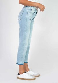 Jeans en denim bleu clair avec une taille haute, une coupe droite et un ourlet effiloché. Comprend des poches arrière avec des détails de couture. Associés à des baskets blanches.