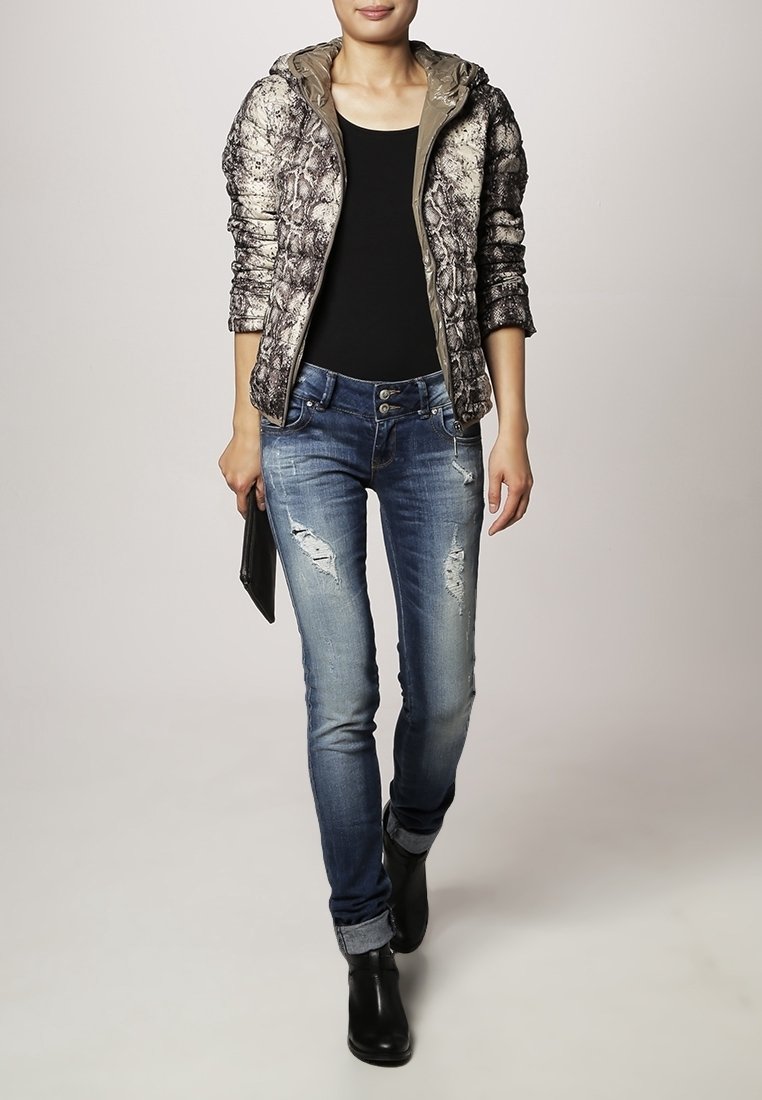 Femme portant une doudoune en peau de serpent, top noir, jeans skinny déchirés, bottes noires, tenant une petite pochette noire, marchant vers l'avant.