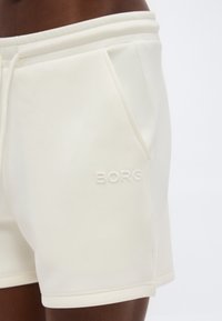 Κοντινό πλάνο ενός ατόμου που φορά ανοιχτόχρωμα σορτς με πλαϊνές τσέπες και ανάγλυφο λογότυπο "BORG" στο αριστερό μηρό.