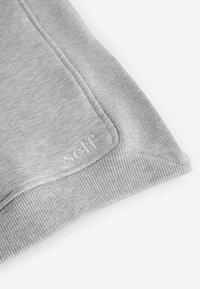 Tessuto grigio della felpa con texture a costine lungo i bordi e design rettangolare. Presenta il logo ricamato "self" vicino alla cucitura.