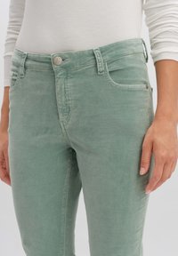 Pantalones de mezcla de algodón verde con una textura suave, que cuentan con un diseño clásico de cinco bolsillos, cierre de botón y detalles de costura sutiles.