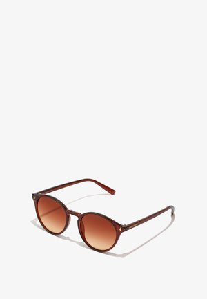 Runde solbriller med en mørkerød plastindfatning og gradient brune linser. Har slanke, buede stænger med gulddetaljer ved hængslerne.