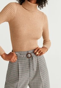 Lichtbruin ribgebreid coltrui gecombineerd met hooggepolsterde plaid broeken met een riem met een ronde gesp en geplooide details.