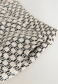 Gros plan sur un tissu tricoté texturé noir et blanc avec un motif ondulé en forme de grille et des détails de points en relief.