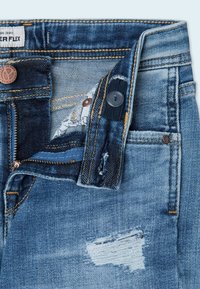 Džínové kalhoty středně modré barvy s distressed záplatou, zapínáním na knoflík a zipem. Vnitřní kapsa má vzorovanou podšívku.