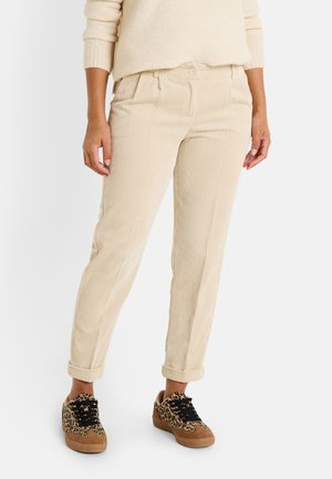 Pantalones de pana beige claro con rayas verticales, de corte relajado y con puños enrollados, combinados con zapatillas deportivas de estampado de leopardo marrón.