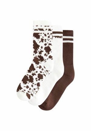Drei Paar Socken: eines mit einem weißen Grund und braunen Kuhflecken, eines einfarbig weiß und eines einfarbig dunkelbraun mit geripptem Muster.