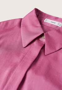 Chemise rose à boutons avec col pointu en tissu doux, montrant le col et la zone du bouton supérieur avec l'étiquette de la marque MNG à l'intérieur.