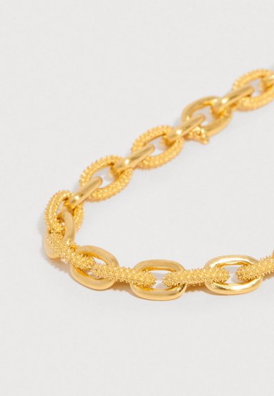 Lănțișor din aur cu zale ovale netede alternând cu zale ovale texturate cu mărgele, pe un fundal deschis.