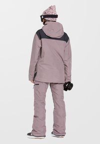 Strój snowboardowy z jasnofioletową kurtką z czarnymi akcentami i dopasowanymi fioletowymi spodniami. Zawiera wzorzysty beanie i rękawice.