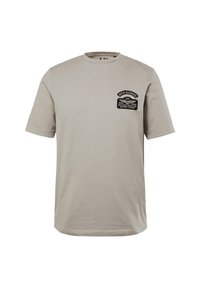 Světle béžové bavlněné tričko s volným střihem. Obsahuje černou grafickou nášivku na hrudi s textem a designovými detaily. S kulatým výstřihem a krátkými rukávy.