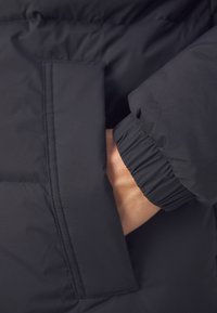 Ręka schowana w kieszeni czarnej kurtki puchowej z elastycznymi ściągaczami rękawów, widok z bliska.