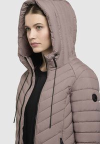Lys mauve pufferjakke med hætte, med lynlås foran, diagonalt quiltet design og sort accentlogo på ærmet.