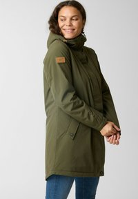 Olijfgroene, waterdichte jas met een hoge kraag en een verwijderbare capuchon. Voorzien van een bruine leren logopatch en drukknopen.