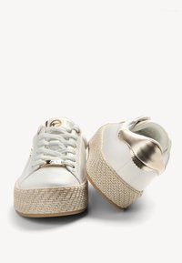 Baskets à plateforme blanches avec semelles texturées tissées, lacets blancs, et accents métalliques dorés sur le talon et l'étiquette des lacets, montrées de face et de dos.