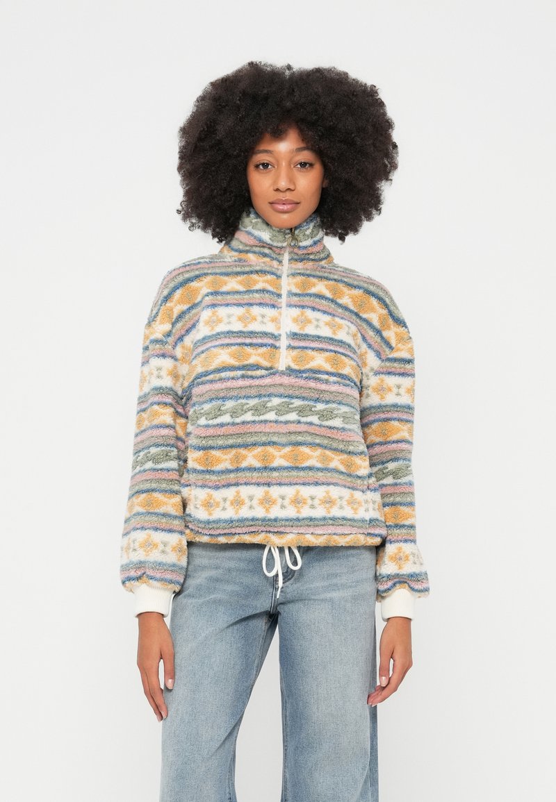 Fliisist pullover kõrge kraega, mitmevärviliste geomeetriliste mustritega, elastse ääre ja nööriga. Pehme tekstuur; põhivärvid on oranž, sinine ja roheline.