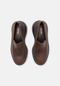 Due scarpe slip-on in pelle marrone con una superficie liscia. Suola in gomma e un marchio discreto visibile all'interno. Design a punta tonda.