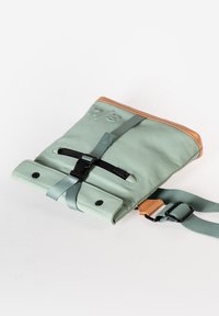 Borsa sintetica verde con dettagli in pelle color nocciola, tracolla regolabile, chiusura arrotolata e fibbia. Texture liscia con accessori neri.