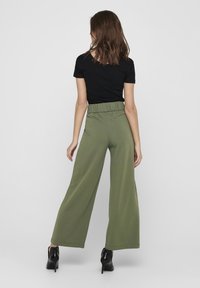 Zelené kalhoty se širokými nohavicemi a elastickým pasem, př paire s přiléhavým černým tričkem. Hladká tkanina, ležérní design. Černé podpatky doplňují vzhled.