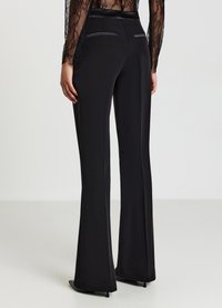 Schwarze, ausgestellte Hosen aus glattem Stoff mit leichtem Glanz, ausgestattet mit einem samtigen Bund und dezenten Details an den Gesäßtaschen.