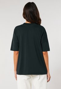 Juodas per didelis marškinėliai trumpomis rankovėmis, apvaliu iškirpimu ir minkšta medvilne; dėvimi su baltais kordūroviniais kelnais. Minimalistinis dizainas.