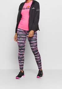 Svart vindjacka, knallrosa t-shirt och mönstrade leggings i rosa och svart. Svarta sneakers med rosa detaljer fullbordar outfiten.