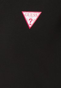 Tejido negro ajustado que presenta un prominente logo triangular rosa con "GUESS" y un signo de interrogación, sobre un fondo de textura acanalada.