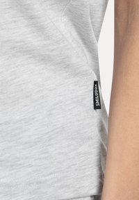 Camiseta de algodón gris claro con una textura suave y una etiqueta de marca negra en la costura lateral. Diseño simple, sin patrones visibles.
