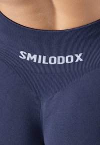 Granatowe legginsy sportowe z żebrowanym paskiem w talii, na którym widnieje napis "SMILODOX" w białym kolorze; gładka faktura i dopasowany fason.