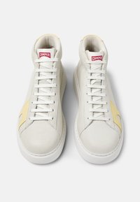 White high-top sneakers with a textured leather exterior, yellow accent on the side, and white laces. Red logo on the tongue.