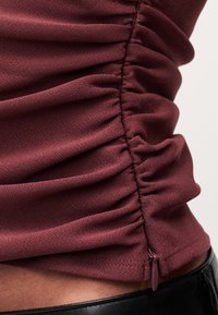 Κοντινή λήψη από μαζεμένο βυσσινί ύφασμα με εμφανές φερμουάρ πάνω στην άκρη μαύρου δερμάτινου ενδύματος.