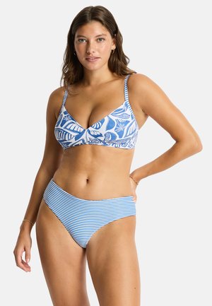 Kobieta nosząca niebiesko-biały wzorzysty stanik od bikini z liśćmi i kwiatowym wzorem oraz niebiesko-białe paski na dole bikini.