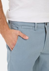 Lichtblauwe denim broek met een gestructureerde afwerking, met een voorzak en een ritssluiting. De tailleband heeft riemlussen en een knoopsluiting.