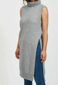 Grå ärmlös polotröja, mjukt stickat material, sidosprund, ribbad krage och nederkant, kombinerad med blå jeans.