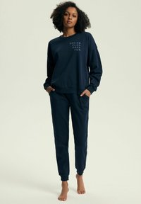 Granatowy dres składający się z bluzy i spodni dresowych; bluza posiada nadruk tekstowy, ściągacze na mankietach i luźny krój; spodnie dresowe są długości ściągacza z elastycznym pasem.