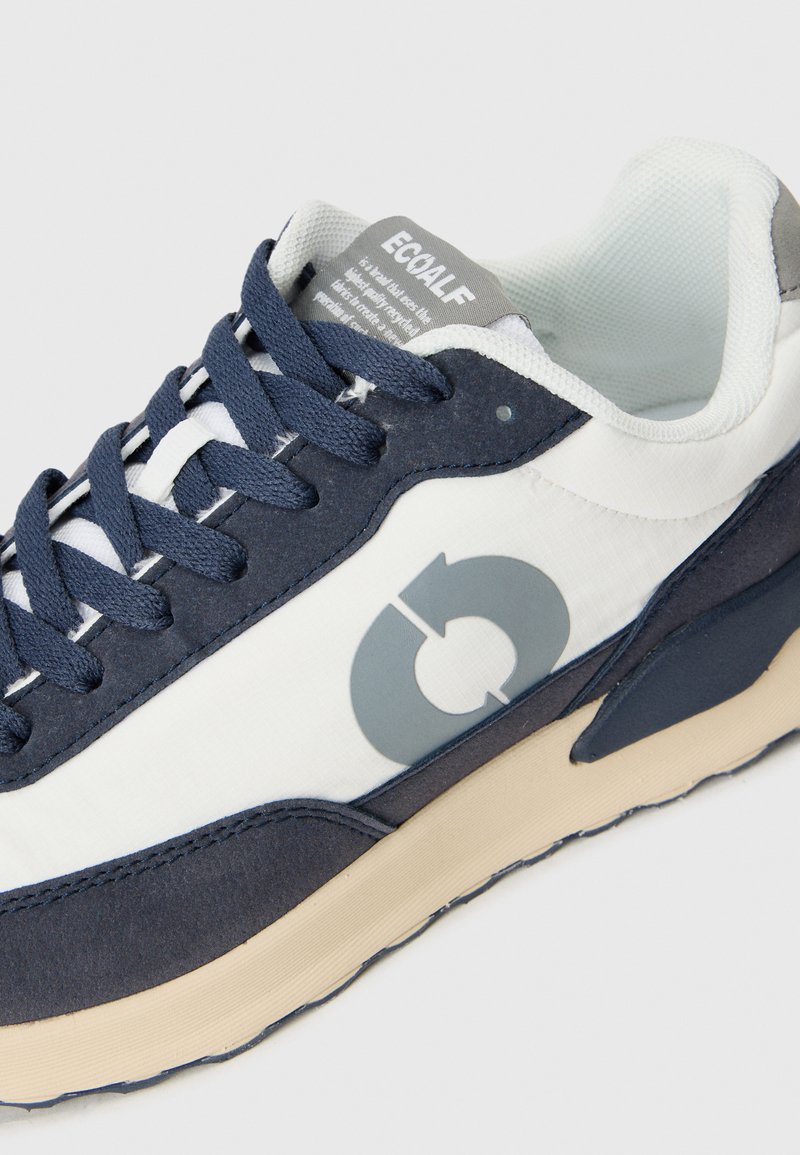 Zapatillas marinas y blancas con un logo gris, tejido texturizado, puntera redonda y cordones planos. Suela de goma duradera con acentos beiges contrastantes.