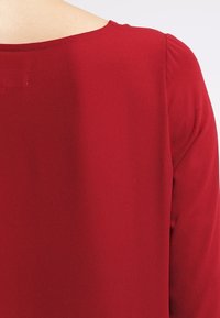 Roter, glatter Stoff mit rundem Ausschnitt, gerafftem Ärmel-Detail, einfarbig und mit subtiler Glanz. Minimalistische Designelemente.