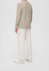 Maglione beige a maglia con maniche lunghe e scollo rotondo; abbinato a pantaloni beige chiaro a gamba larga e scarpe bianche. Texture sottile visibile.