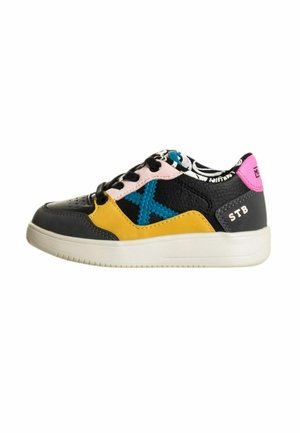 Zapatilla de cuero negro con acentos amarillos y azules, lengüeta en talón rosa y un interior con patrón. Presenta costuras en contraste y una superficie texturada.
