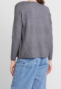 Pull gris avec un motif de tricot texturé, coupe ample et manches longues, associé à un jean en denim clair taille haute.