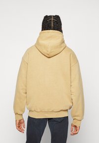 Sudadera oversize beige con una gran capucha, mangas elásticas y con puños, y una textura suave. La parte posterior presenta un diseño simple y sin costuras.