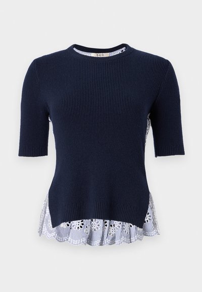 Marineblauwe geribbelde trui met korte mouwen en een gelaagde witte en blauwe gestreepte ruffle onderkant met bloemen uitsparingen. Zachte textuur, casual ontwerp.