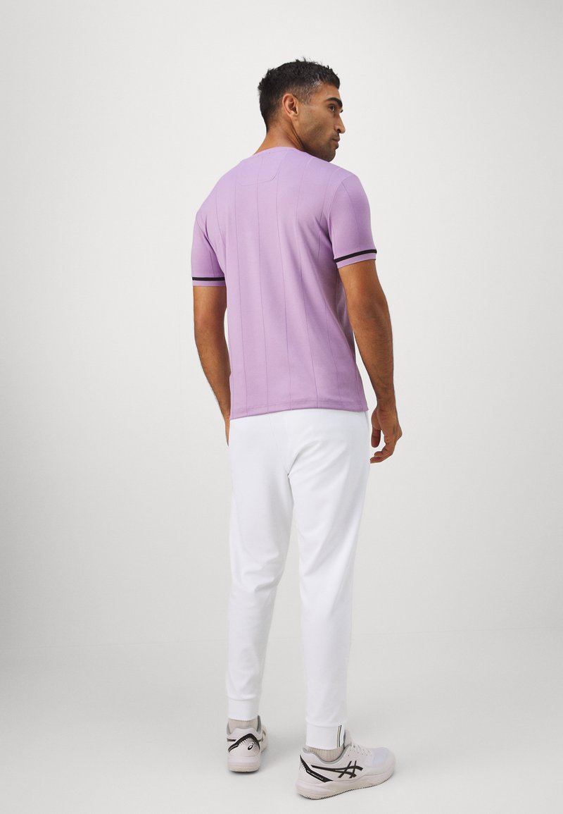 Lavendelkleurig poloshirt met korte mouwen en zwarte afwerking, met naaddetails, gecombineerd met witte broeken en schoenen in lichte kleuren.