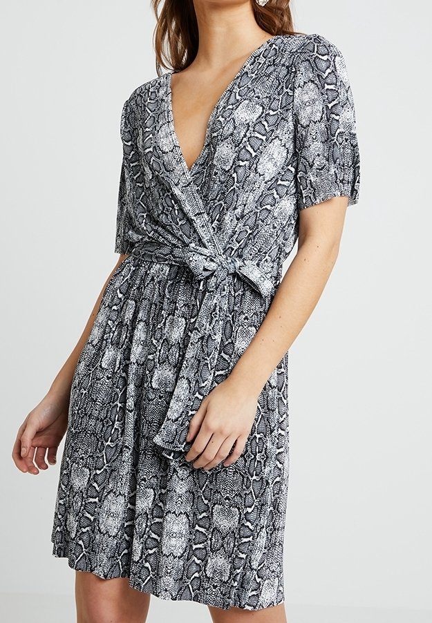 Vestido de estampado de serpiente en blanco y negro, con mangas cortas, un escote en V profundo y un detalle de cintura anudada. Presenta una falda fluida.