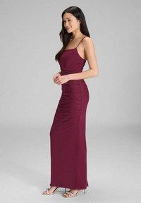 Bordeaux Maxikleid mit Spaghettiträgern, gerüschtem Design, taillierter Passform und bodenlangem Schnitt. Sandalen mit betontem dünnem Absatz.