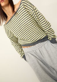 Gestreifter Pullover in Gelb und Grau mit einem schulterfreien Design, kombiniert mit grauen Jogginghosen mit elastischem Bund und Rüschensaum.