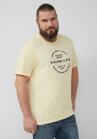 Lichtgele katoenen t-shirt met een ronde bedrukte logo met tekst in marineblauw, korte mouwen en een ronde hals. Draag het met blauwe spijkerbroeken.