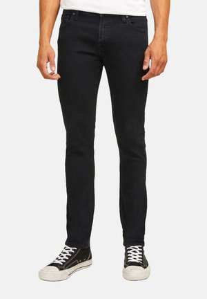 Jeans in denim nero con vestibilità slim, dotati di un classico design a cinque tasche e zip, abbinati a sneaker alte nere.