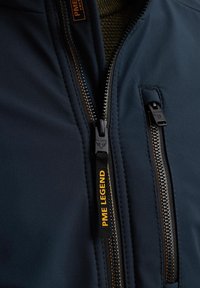 Navy Softshell-Jacke mit auffälligen Reißverschlüssen, einem PME Legend-Label, strukturiertem Gewebe und kontrastierenden orangen Akzenten.